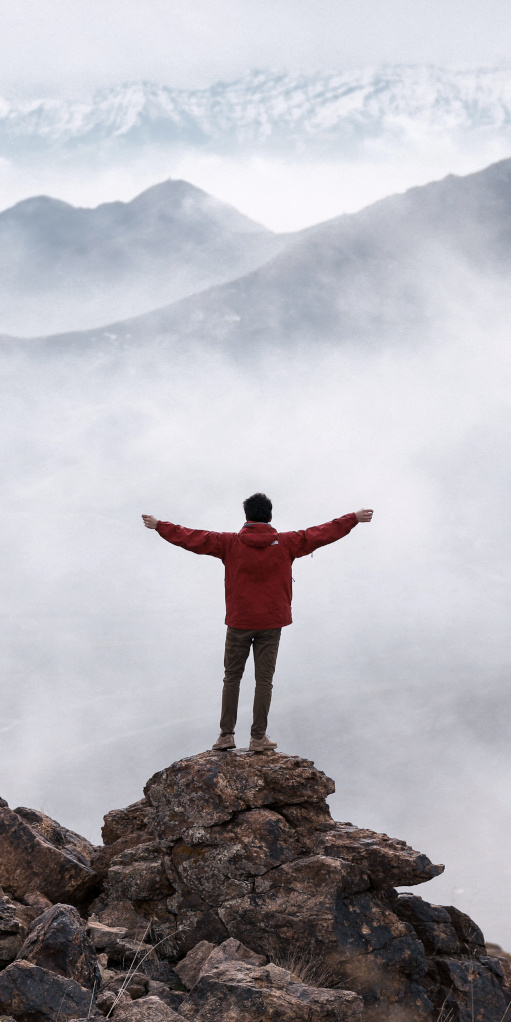 Junger Mann steht auf einem Berg und blickt in die Weite.