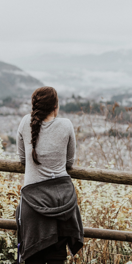 Junge Frau von hinten, die bei einer Auszeit im Retreat mit einem Kaffee in der Hand von einer Anhöhe in die Natur blickt